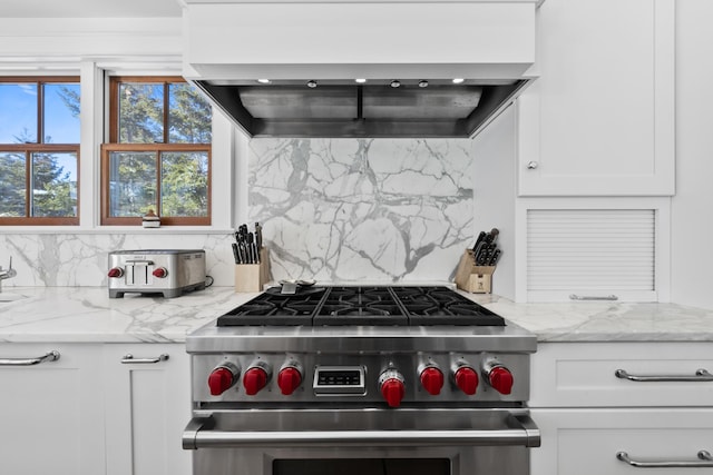 kitchen with white cabinets, high end stainless steel range oven, backsplash, custom exhaust hood, and light stone countertops