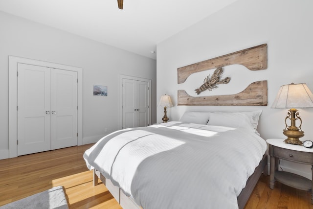 bedroom with ceiling fan, light wood-style flooring, baseboards, and two closets