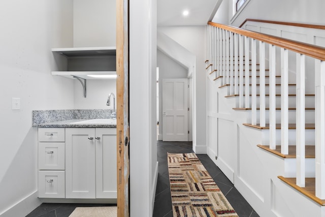 interior space featuring baseboards, stairway, dark tile patterned floors, a sink, and recessed lighting