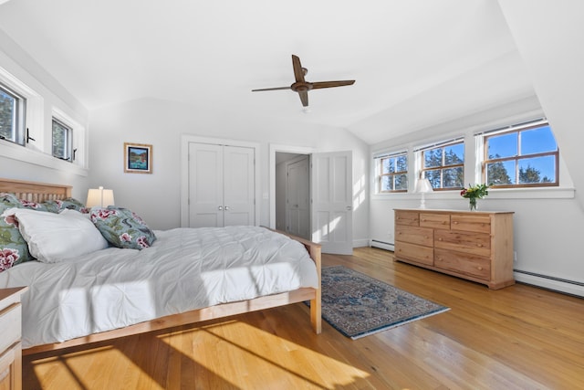 bedroom with lofted ceiling, light wood-style flooring, baseboard heating, and a closet