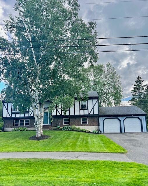 tudor home with a front lawn, an attached garage, brick siding, and aphalt driveway