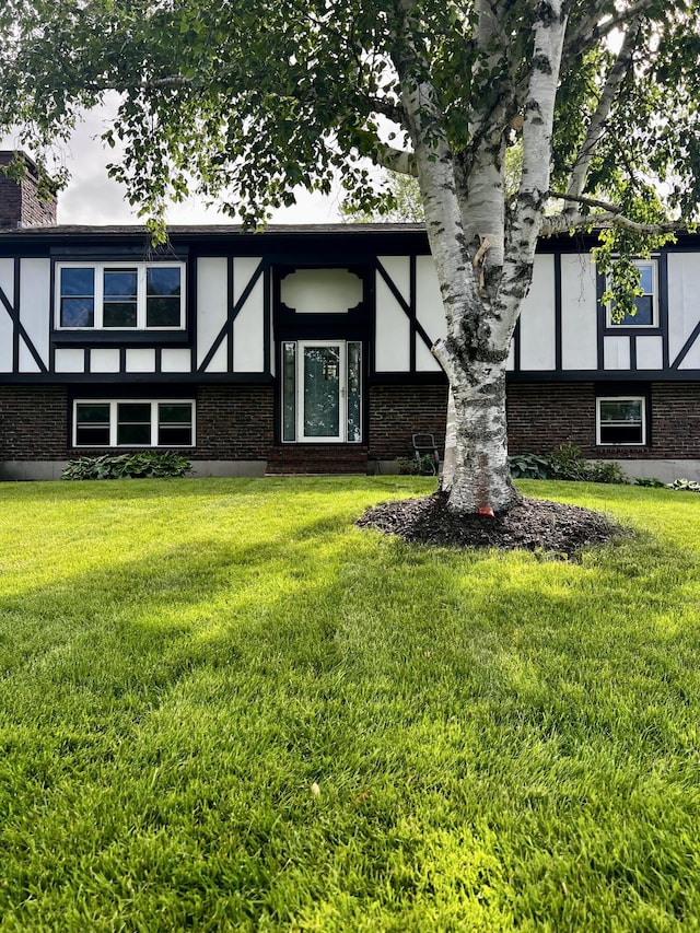 view of front facade featuring a front lawn, a chimney, brick siding, and stucco siding