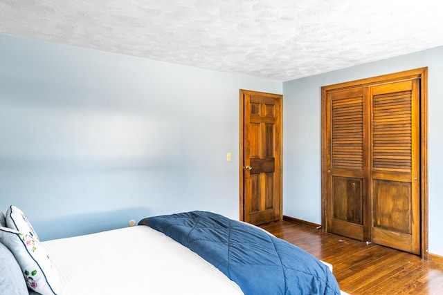 bedroom featuring dark wood-style floors, a closet, a textured ceiling, and baseboards