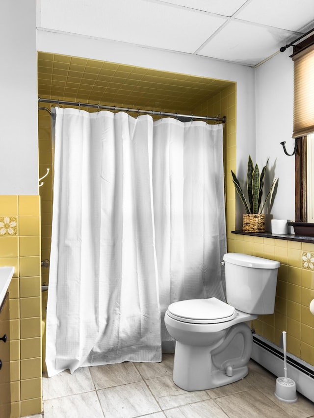 bathroom featuring a baseboard heating unit, toilet, a shower with shower curtain, and tile walls