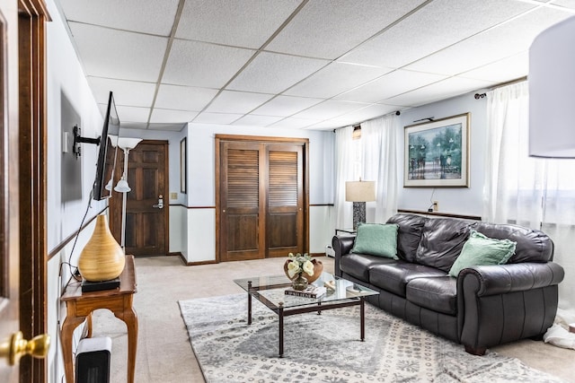 living area with a paneled ceiling, light colored carpet, and baseboards