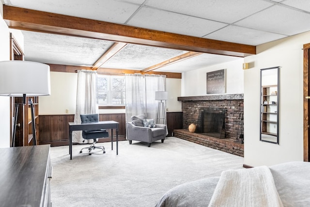 living room featuring a paneled ceiling, a brick fireplace, beamed ceiling, and light colored carpet