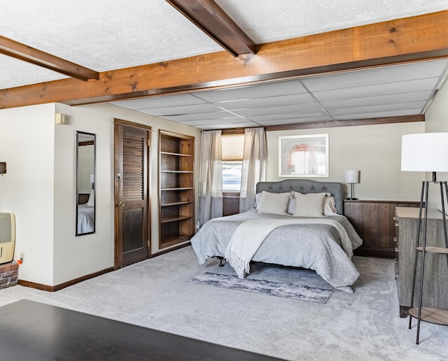 bedroom with a textured ceiling, beamed ceiling, carpet, and baseboards