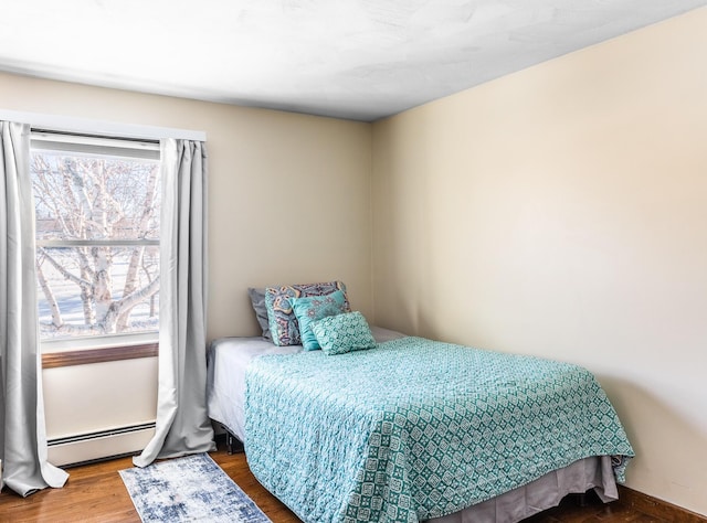 bedroom featuring a baseboard heating unit, multiple windows, and wood finished floors