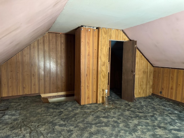 additional living space with dark colored carpet, vaulted ceiling, and wooden walls