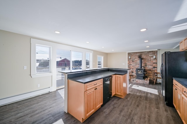 kitchen with dark wood-style flooring, dark countertops, a baseboard radiator, a wood stove, and black appliances