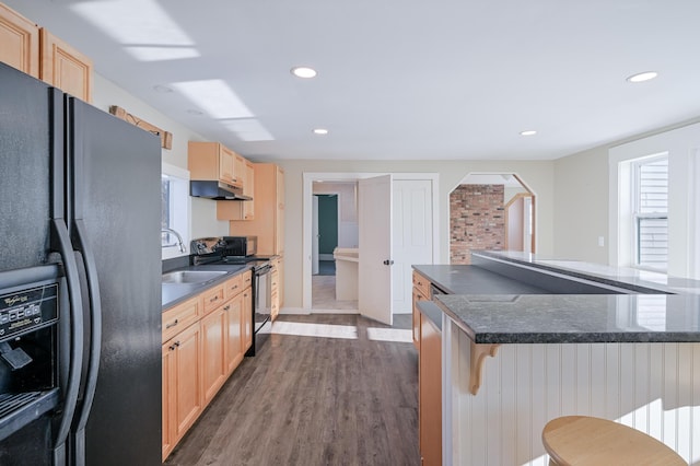 kitchen featuring a breakfast bar, dark countertops, a sink, under cabinet range hood, and black appliances