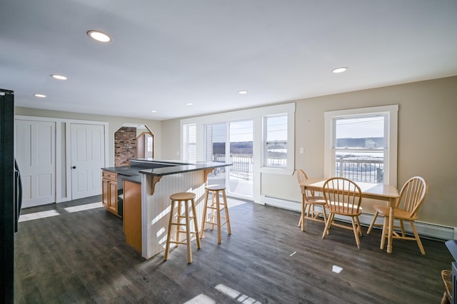 kitchen with arched walkways, dark countertops, a kitchen island, dark wood-type flooring, and a kitchen bar