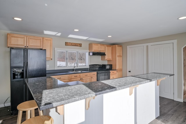 kitchen featuring a kitchen island, a breakfast bar, a sink, and black appliances