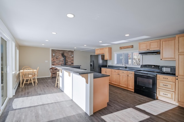 kitchen with a breakfast bar area, dark countertops, a sink, under cabinet range hood, and black appliances