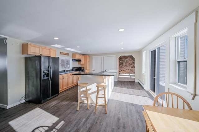 kitchen with dark countertops, a breakfast bar, black fridge, and light brown cabinetry