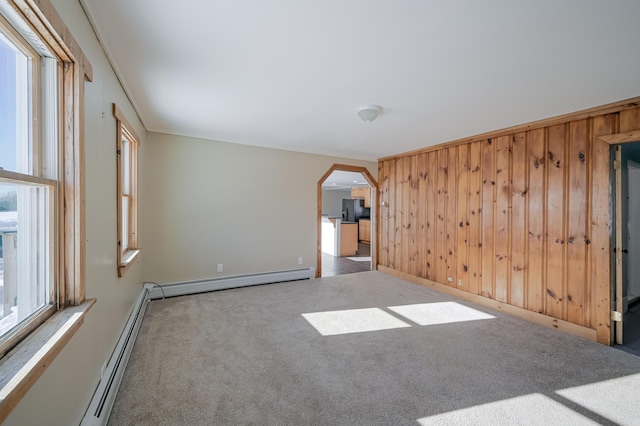 carpeted spare room featuring arched walkways, a baseboard radiator, wood walls, ornamental molding, and baseboard heating