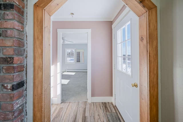 interior space featuring a baseboard heating unit, light carpet, baseboards, ornamental molding, and light wood finished floors