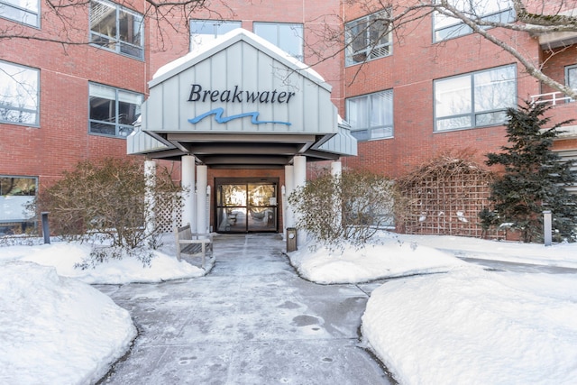 snow covered property entrance featuring brick siding