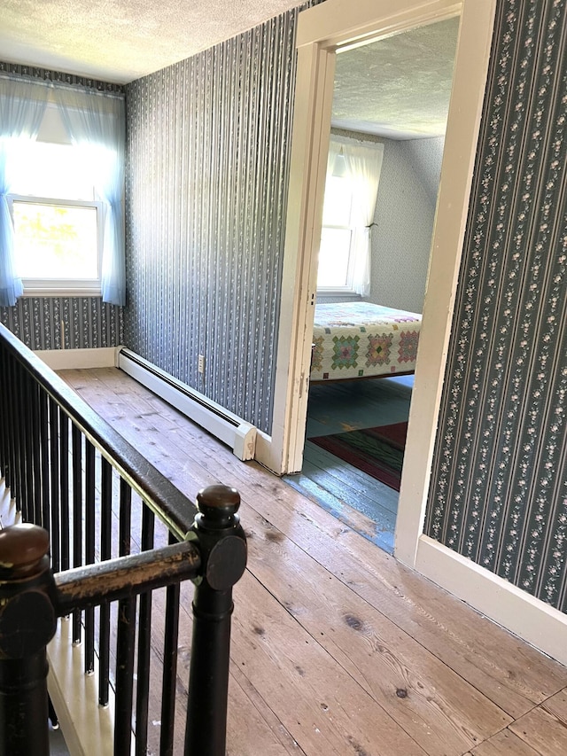 96 Exeter Rd, Garland, ME 04939 - staircase with wallpapered walls, a baseboard heating unit, wood-type flooring, plenty of natural light, and a textured ceiling