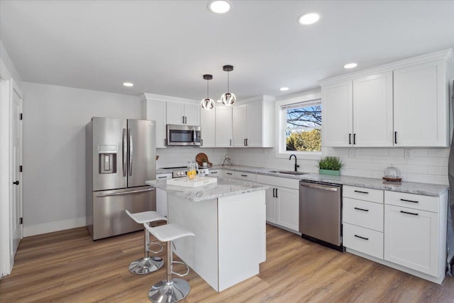 kitchen featuring a center island, decorative light fixtures, appliances with stainless steel finishes, white cabinetry, and a sink