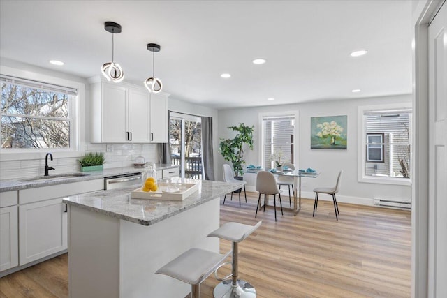 kitchen with a baseboard radiator, light stone counters, hanging light fixtures, white cabinetry, and a sink