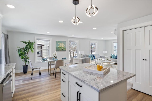 kitchen featuring a center island, pendant lighting, stainless steel dishwasher, white cabinets, and light stone countertops