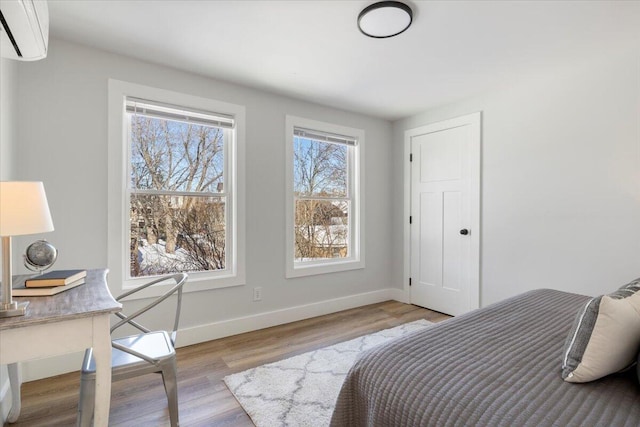 bedroom with a wall unit AC, light wood-style flooring, and baseboards