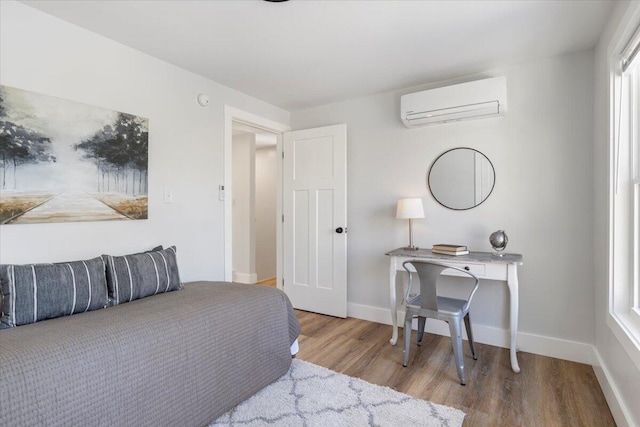 bedroom featuring an AC wall unit, light wood-style flooring, and baseboards