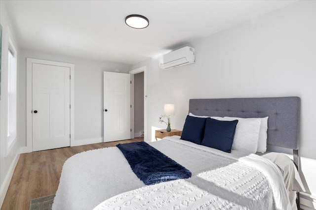 bedroom featuring an AC wall unit, light wood finished floors, and baseboards