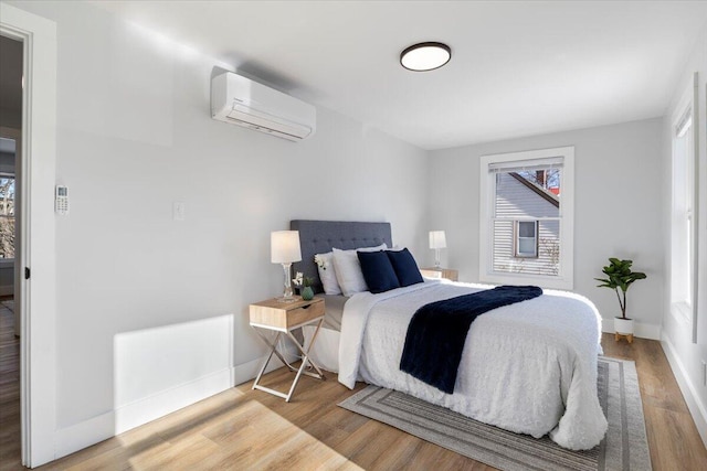 bedroom with baseboards, an AC wall unit, and light wood-style floors