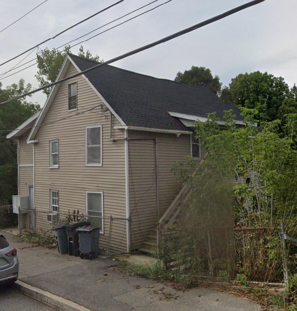 view of side of property with a shingled roof, fence, and stairway