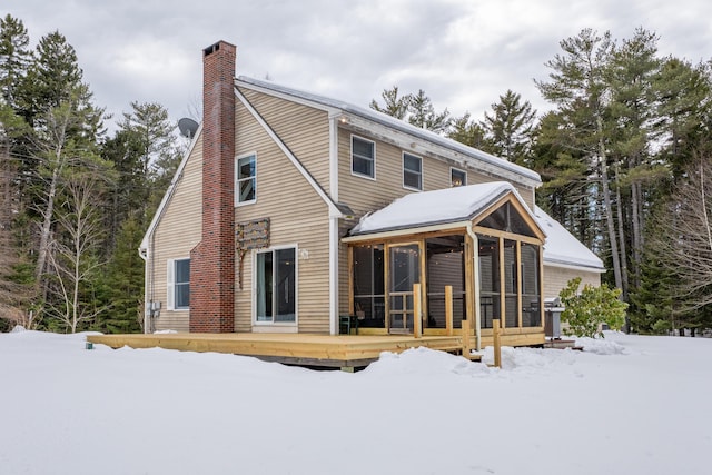 snow covered back of property with a chimney, a wooden deck, and a sunroom