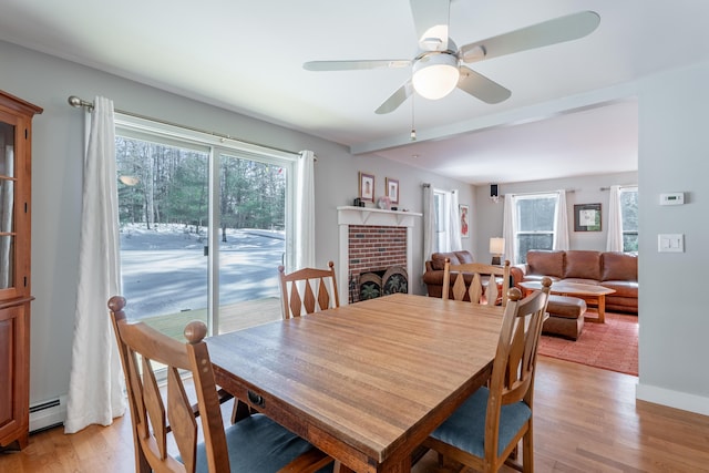 dining space with a brick fireplace, a baseboard radiator, plenty of natural light, and light wood finished floors