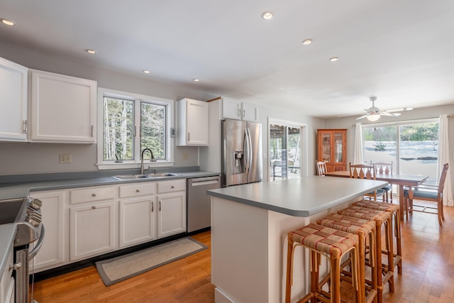 kitchen with appliances with stainless steel finishes, a breakfast bar, light wood-style floors, white cabinetry, and a sink