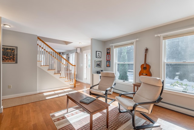 living area featuring light wood-style flooring, stairs, a baseboard heating unit, and baseboards