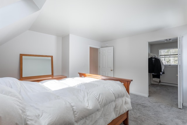 bedroom with a baseboard heating unit, light colored carpet, vaulted ceiling, and baseboards