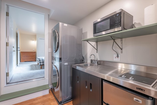 laundry room with light wood-type flooring, stacked washer / drying machine, laundry area, and a sink