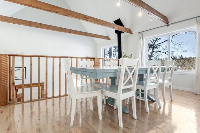 dining area featuring lofted ceiling with beams, wood finished floors, a wood stove, and rail lighting