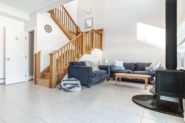 living room featuring a towering ceiling, a wood stove, stairs, and light tile patterned flooring