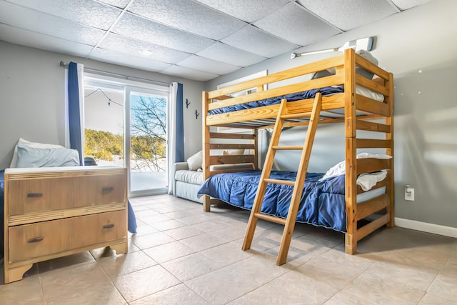 bedroom featuring light tile patterned floors, access to outside, baseboards, and a drop ceiling