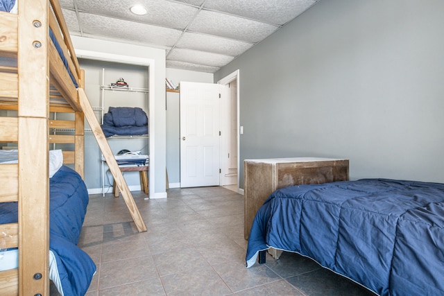 bedroom featuring a drop ceiling, tile patterned flooring, and baseboards