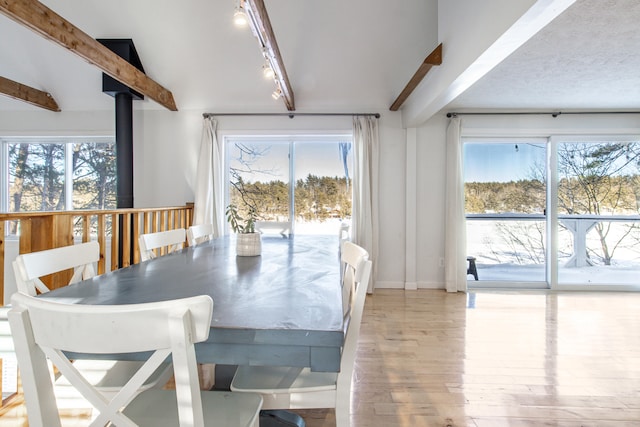dining room with a healthy amount of sunlight, light wood-type flooring, and beamed ceiling