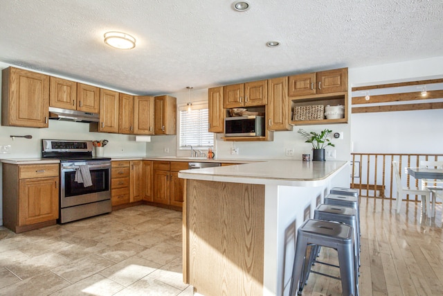 kitchen featuring appliances with stainless steel finishes, a peninsula, light countertops, under cabinet range hood, and a kitchen bar