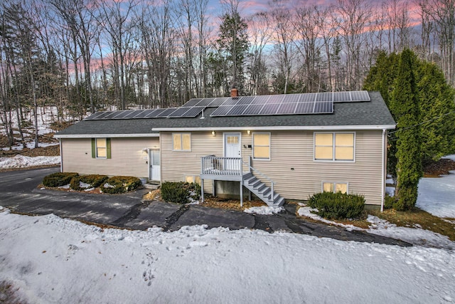 rear view of property with solar panels, a chimney, and roof with shingles