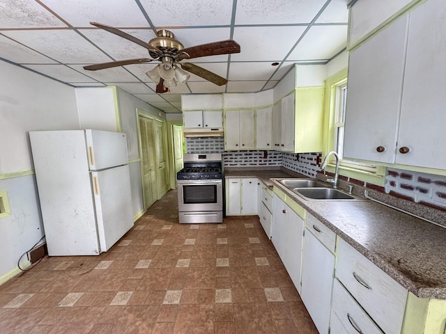 kitchen featuring a paneled ceiling, white appliances, a sink, decorative backsplash, and dark countertops