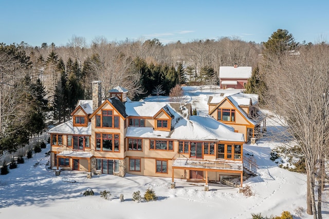 snow covered rear of property featuring a chimney and a wooded view