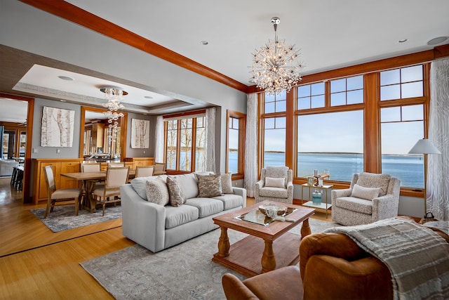 living area featuring a water view, light wood-style floors, a chandelier, and a raised ceiling