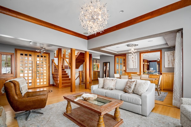 living room with a tray ceiling, light wood finished floors, stairway, an inviting chandelier, and plenty of natural light