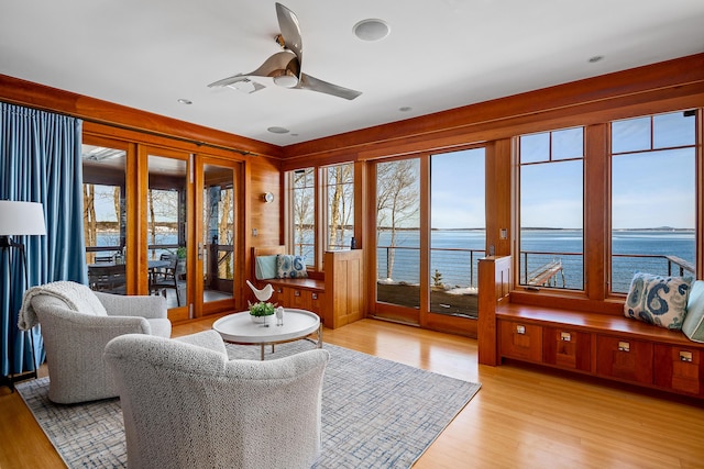 living area with a water view, light wood-style flooring, and a ceiling fan