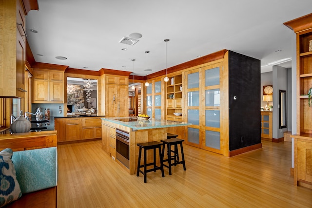 kitchen with black electric stovetop, stainless steel oven, visible vents, light wood finished floors, and a kitchen bar